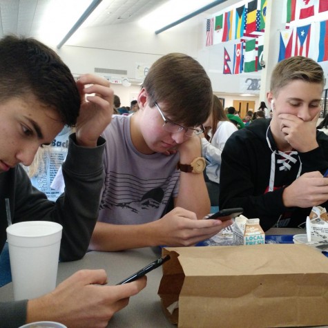 three seniors sit on their phones at lunch.