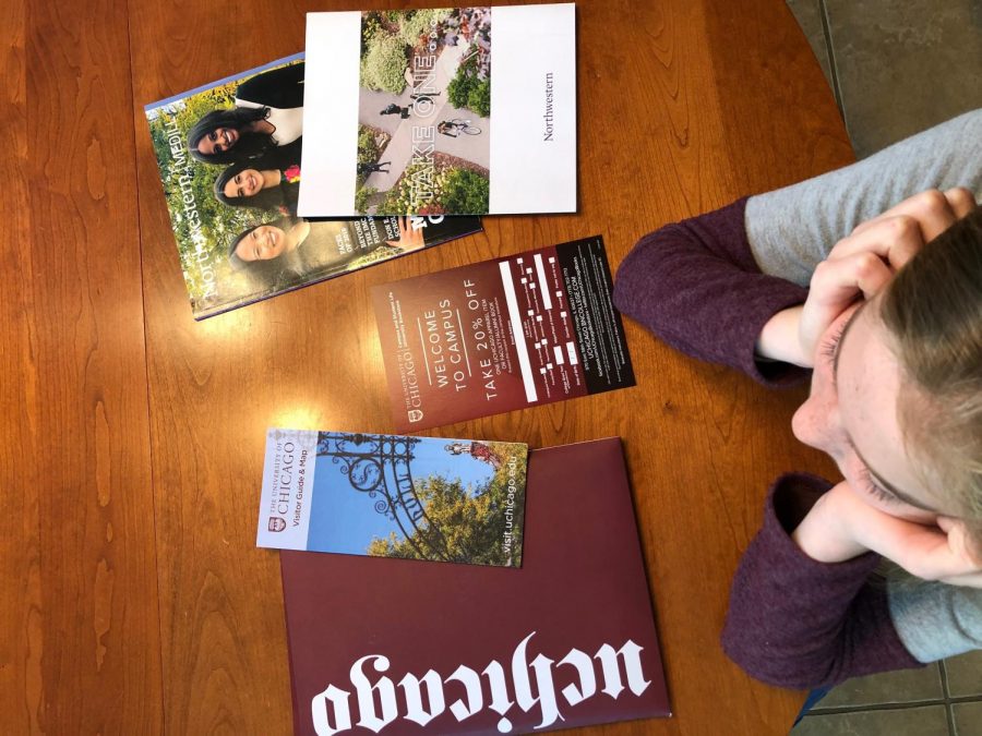 A student is surrounded by informational packets and maps from college visits.