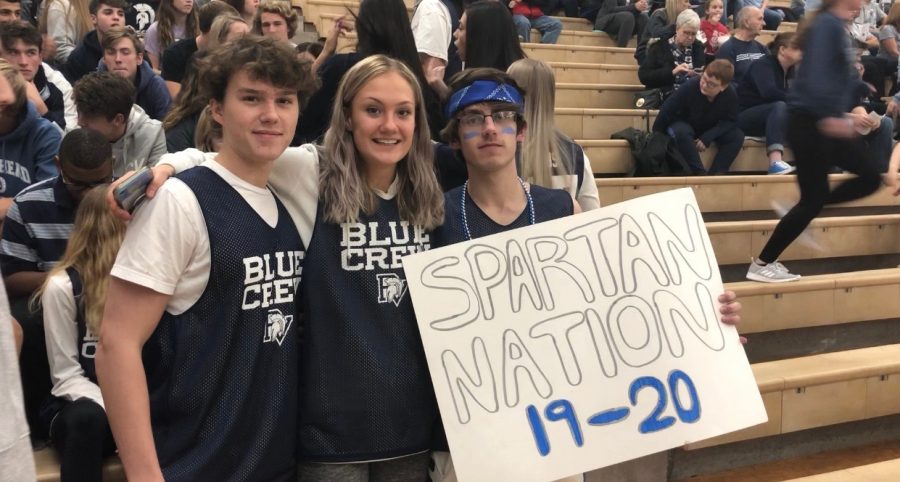 Seniors Matthew Brewster, Megan Gropel, and Andrew Doyle hold up a sign in their blue crew jerseys for the last home volleyball game.