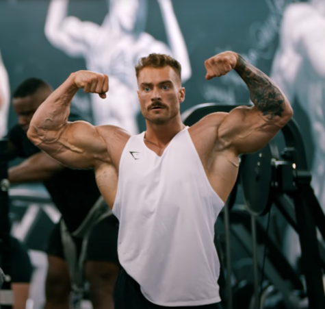 Chris Bumstead, 3x Mr. Olympian and a popular influencer, flexes in front of a camera.