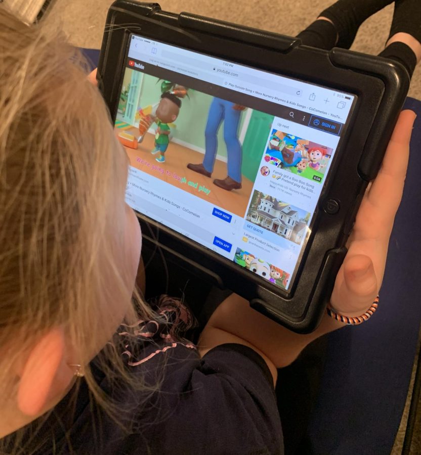 A young girl is featured intently watching videos by the channel “Cocomelon” on her iPad. 
