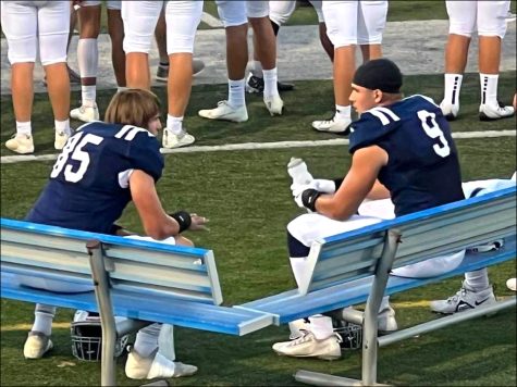 Andrew and William DePaepe sitting on sidelines talking at varsity football game against Cedar Rapids Prairie.
