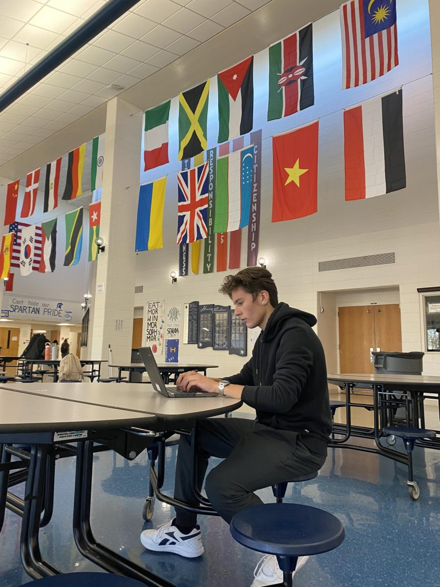 Junior Andres Bravo Garza works on his assignments under 30 flags in the PVHS cafeteria that represent the nationalities of international PV students.