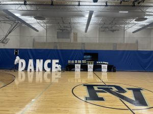 The backdrop for the dance competition is set, showcasing various awards. Dancers perform their routines in the main gym.