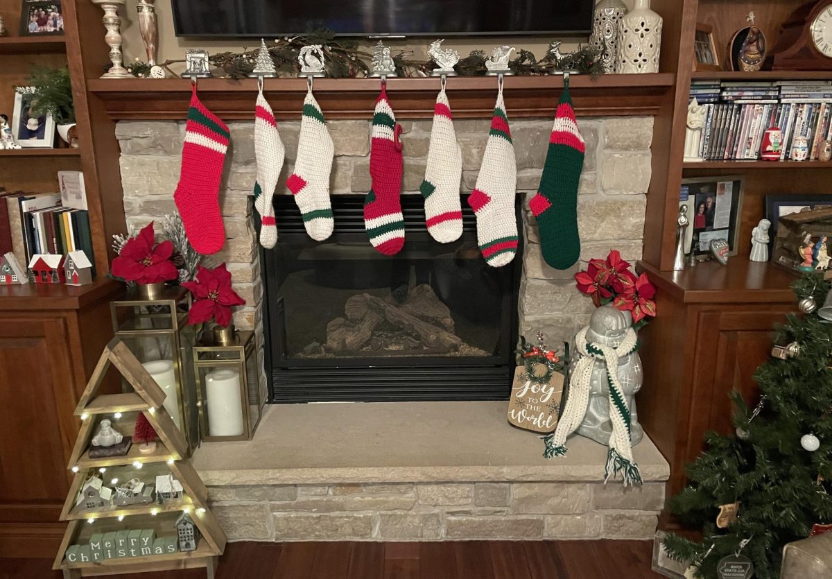 A fireplace is decorated with red and green stockings, poinsettias and trees to match the traditional Christmas theme.

